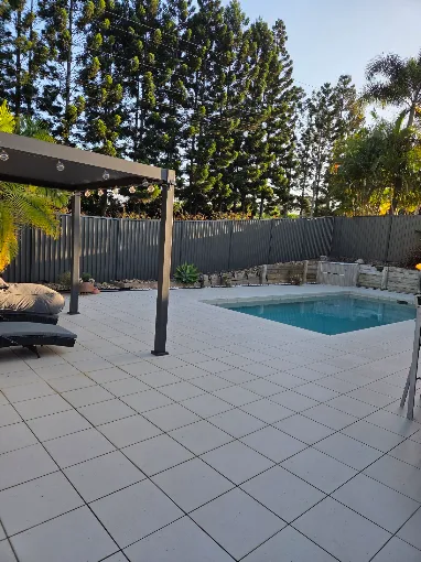Grey Colorbond pool fence around a tiled pool with pergola and daybed