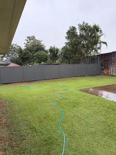 Long grey Colorbond fence line across a rear yard on a rainy Sunshine Coast day