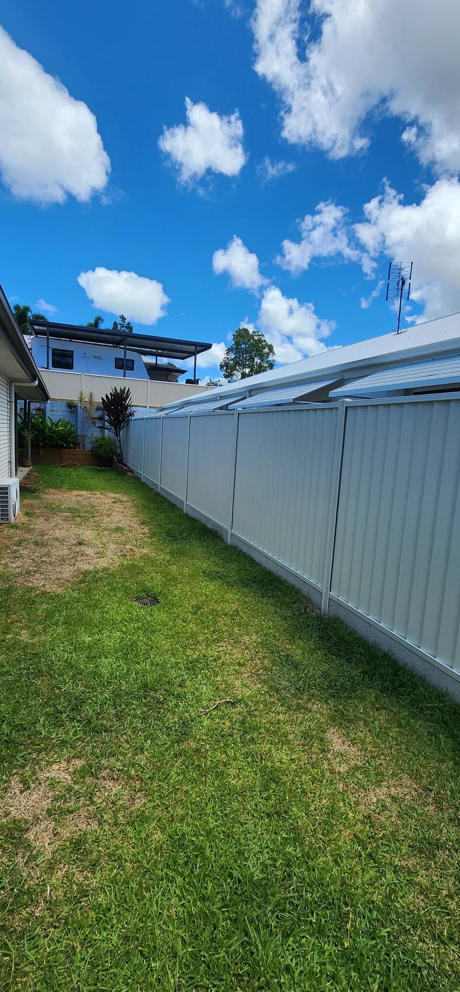 Long run of grey Colorbond side fence on green lawn under a bright Sunshine Coast sky